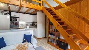 A modern kitchen with white cabinets, a microwave, and a sink. There's a wooden staircase with a built-in shelf. - Cosy apartment for 5 people with WIFI, TV and terrace (La Palmyre)