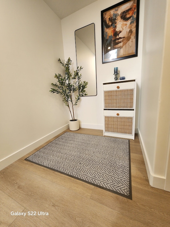 A hallway with a Galaxy S22 Ultra rug, a potted plant, a mirror, and a white cabinet with decorative items. - Cozy Indigo retreat-Two Bedroom -private Entrance-pet Friendly
(Beaumont)