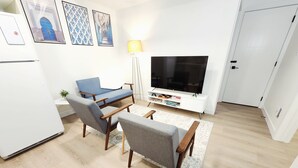 Ett modernt vardagsrum med en platt-TV, två fåtöljer, ett soffbord och en golvlampa.