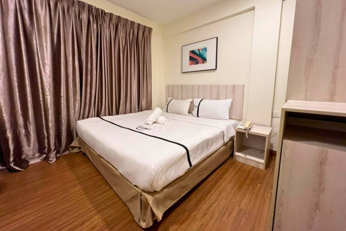 Een hotelkamer met een groot bed, een nachtkastje met een telefoon en een schilderij aan de muur.