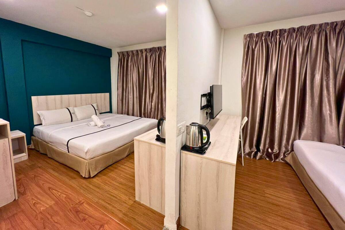 Een hotelkamer met een bed, een bureau met waterkoker, een televisie en gordijnen.