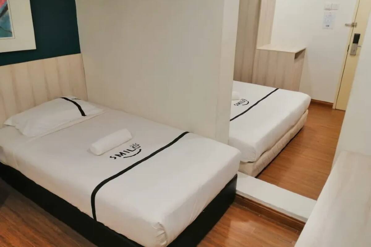 Een hotelkamer met twee eenpersoonsbedden, elk met een witte matras en een zwart hoofdeinde.