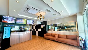 A hotel lobby with a reception desk, a sofa, a kitchen area, and a TV screen displaying a cityscape. - Smile Hotel Cheras Taman Segar (Kuala Lumpur)