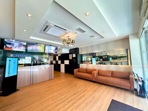 Eine Hotelhalle mit einer Rezeption, einer Sitzecke, einer Küchenzeile und einem Fernseher, der eine Stadtansicht zeigt.