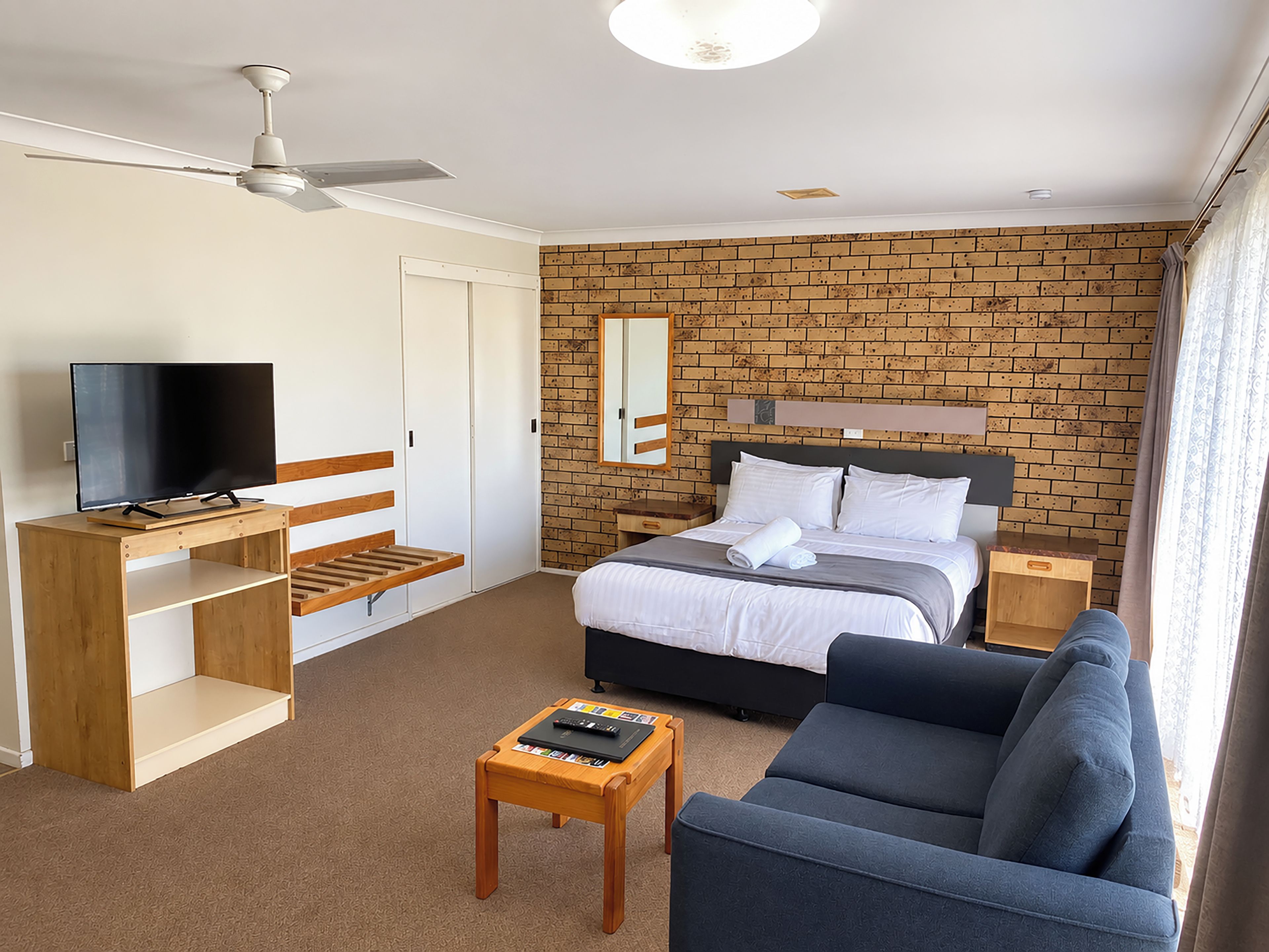 A hotel room with a bed, a TV, a desk, a sofa, and a brick wall.