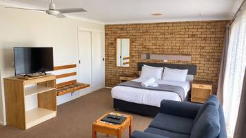 A hotel room with a bed, a TV, a desk, a sofa, and a brick wall.