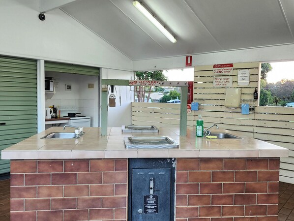 Un'area cucina esterna pulita e ben curata, con un bancone in mattoni, lavelli in acciaio inossidabile e una griglia barbecue.