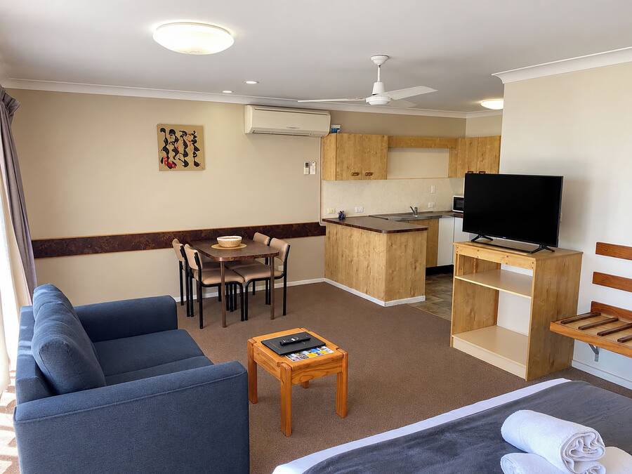 Un espacio habitable compacto con un sofá, una pequeña mesa de comedor, un televisor y una kitchenette.