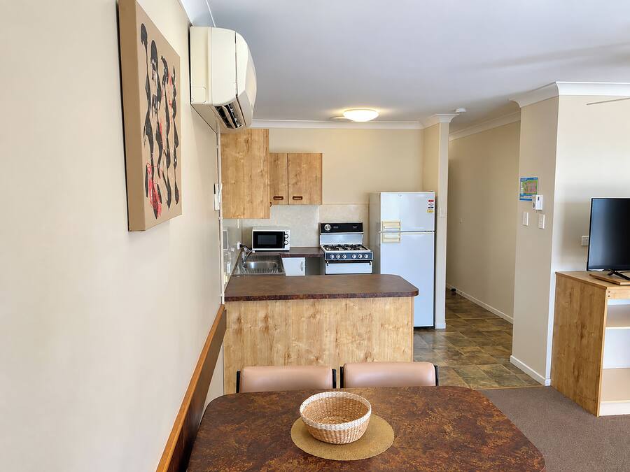 A compact kitchen with a microwave, stove, and refrigerator. There is a dining table with a basket and chairs.