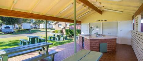 A covered outdoor area with picnic tables, a kitchen, and a view of the surrounding area.