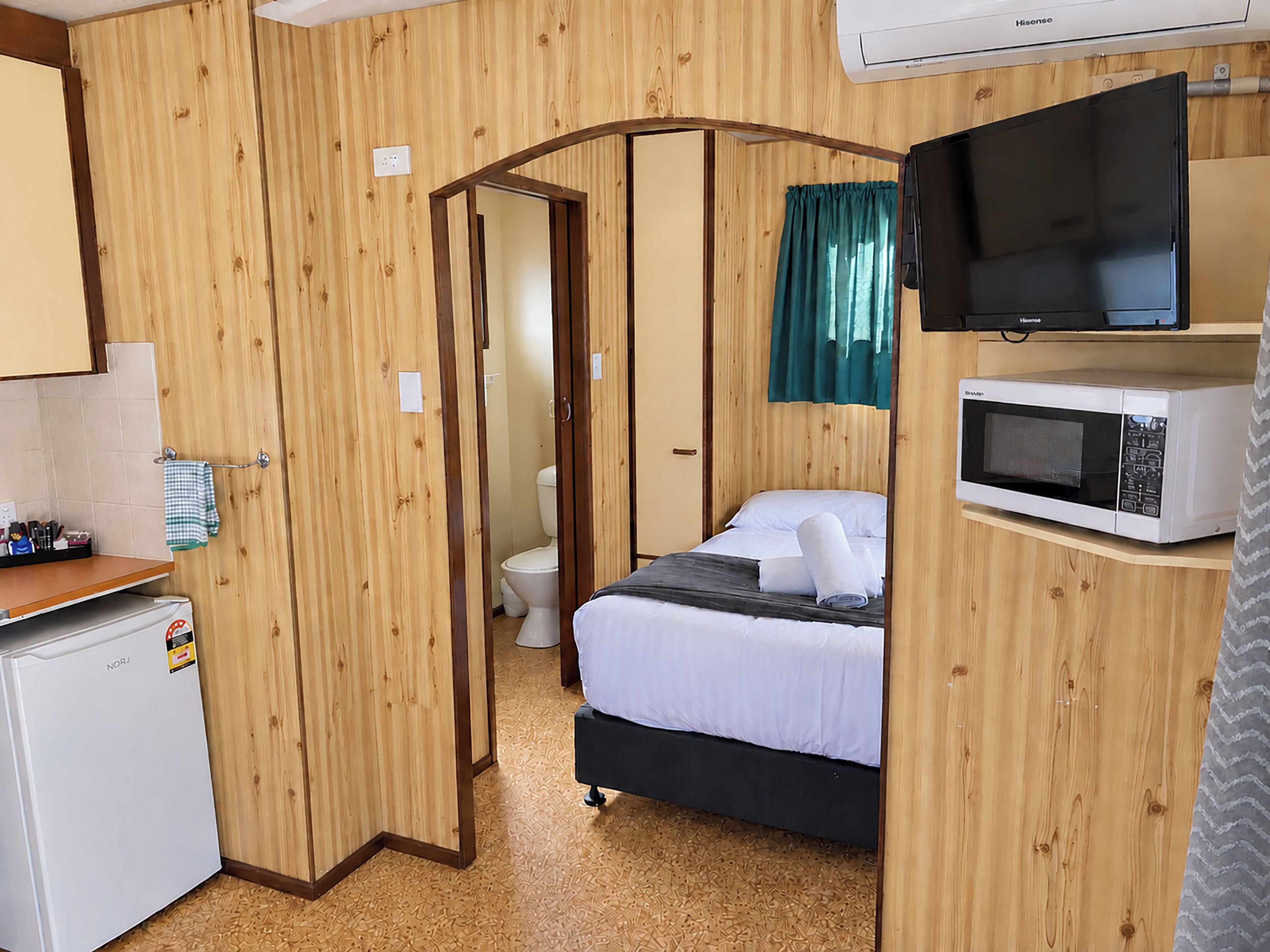 A compact room with a bed, a microwave, a television, and a small refrigerator.