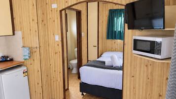A compact room with a bed, a microwave, a television, and a small refrigerator.