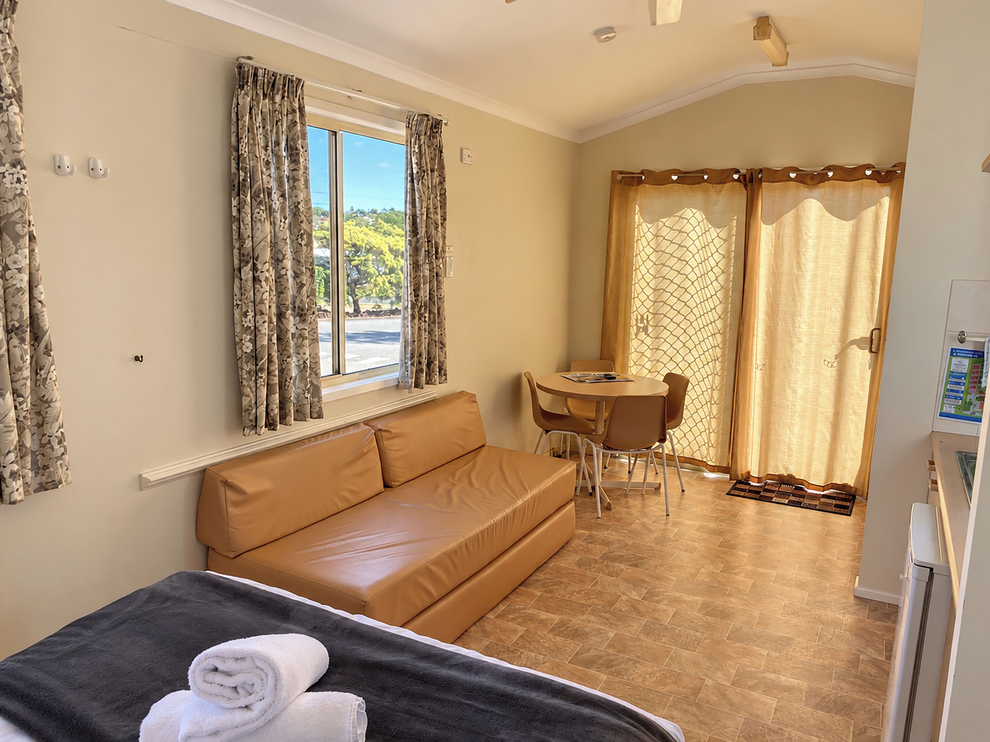 A room with a bed, a sofa, a dining table with chairs, and a view of the outdoors through a window.