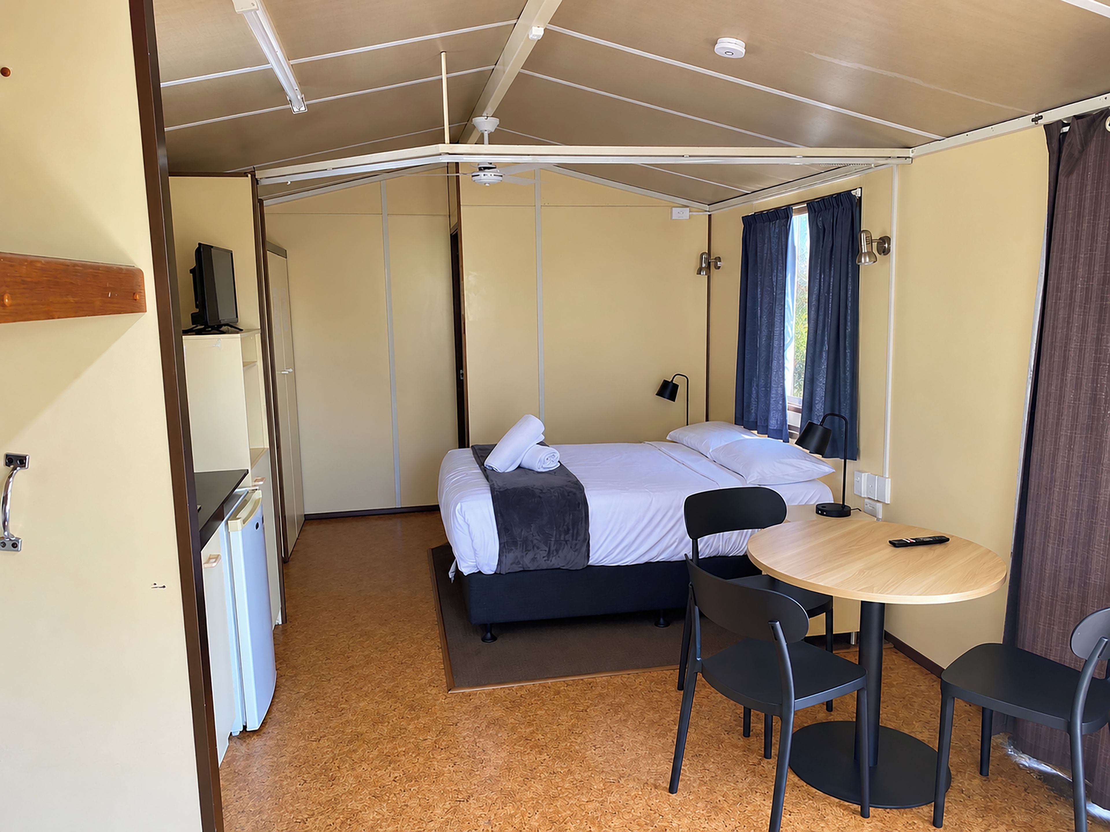 A compact room with a bed, a small table, and chairs, a television, and a window with curtains.