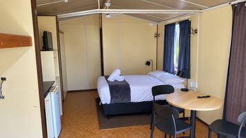 A compact room with a bed, a small table, and chairs, a television, and a window with curtains.