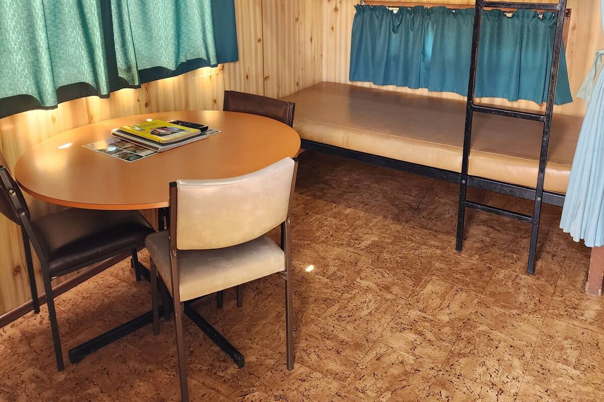 A bunk bed with curtains, a round table with chairs, and a bulletin board.