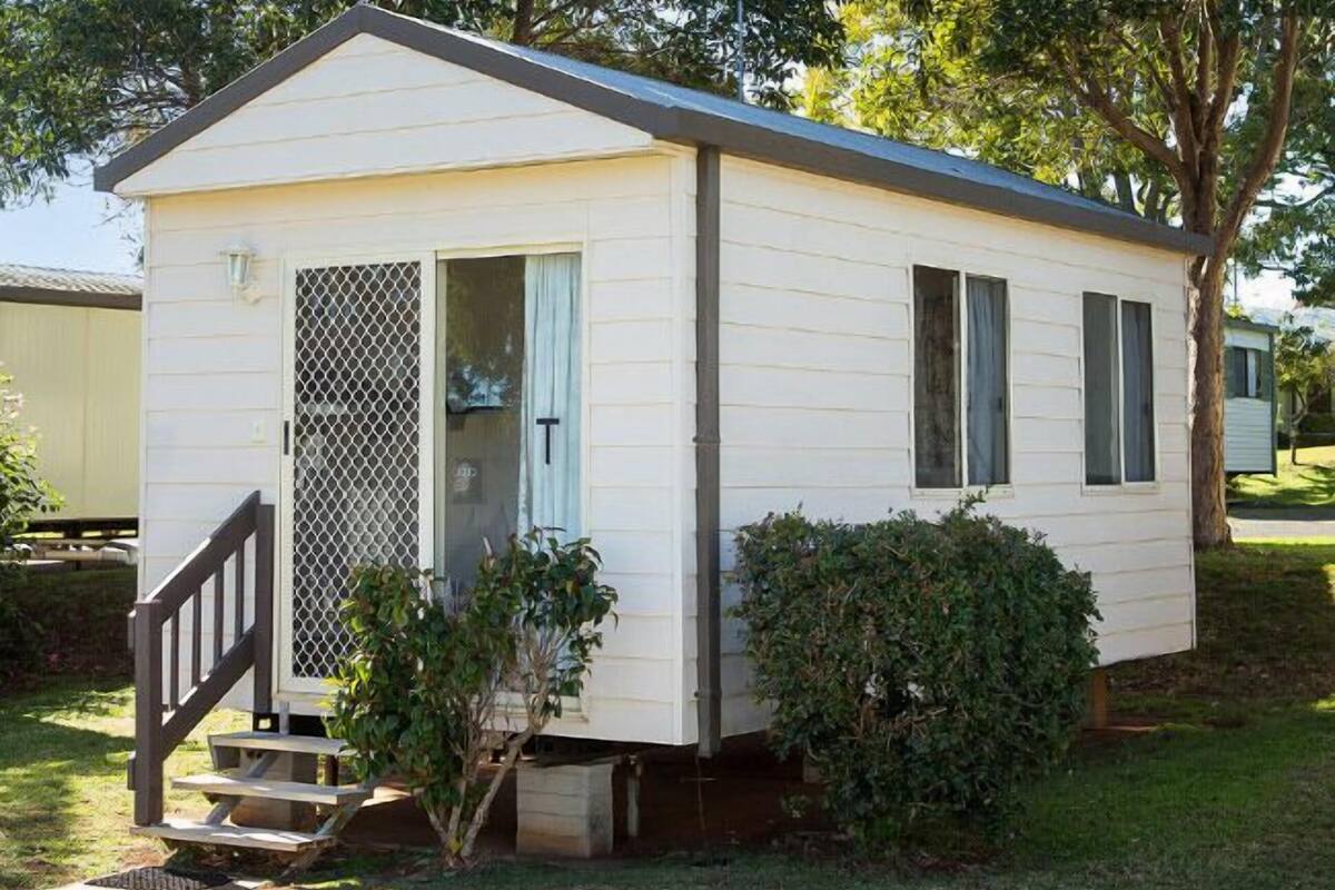 A small, single-story mobile home with a front porch and a screened door.