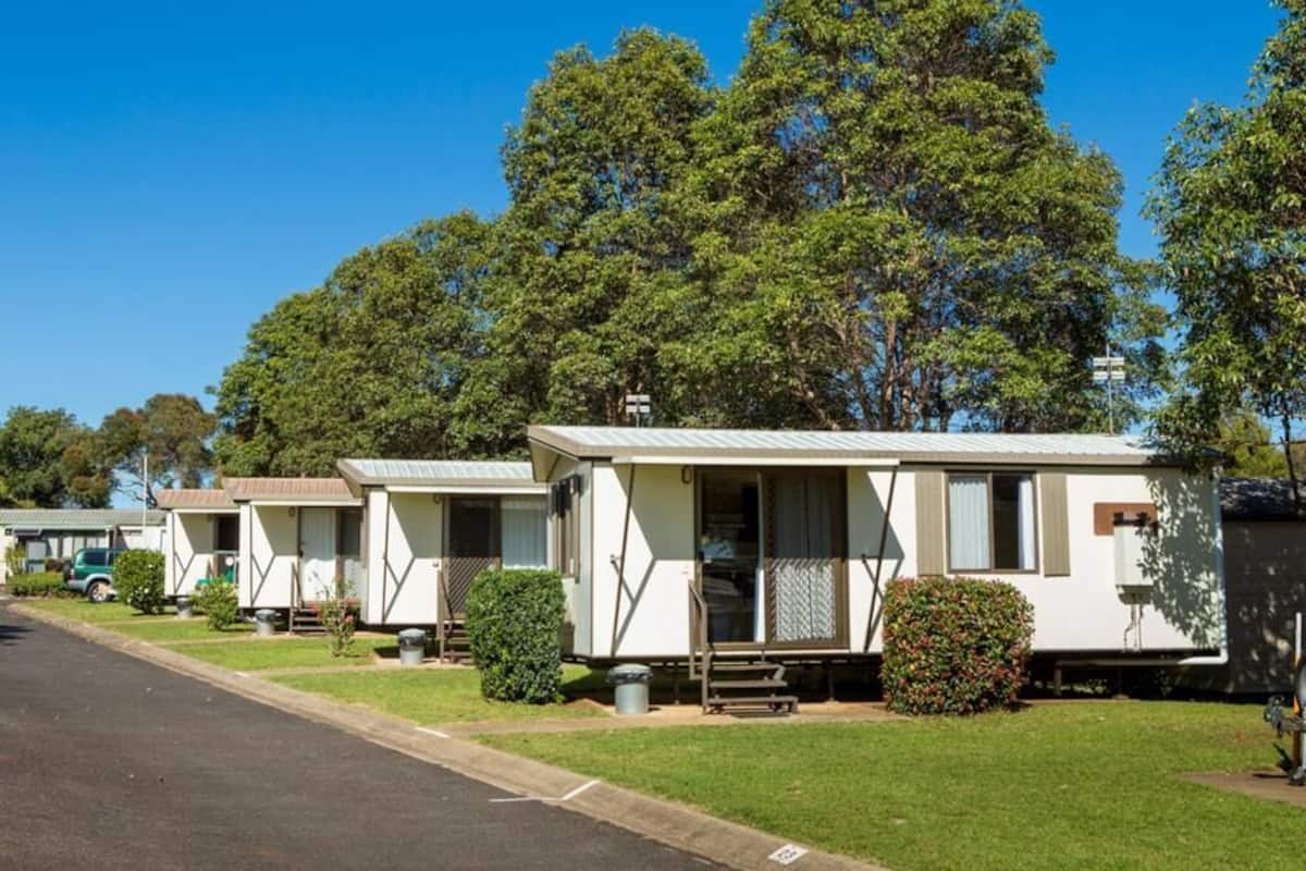 A row of mobile homes with a grassy lawn and trees in the background.