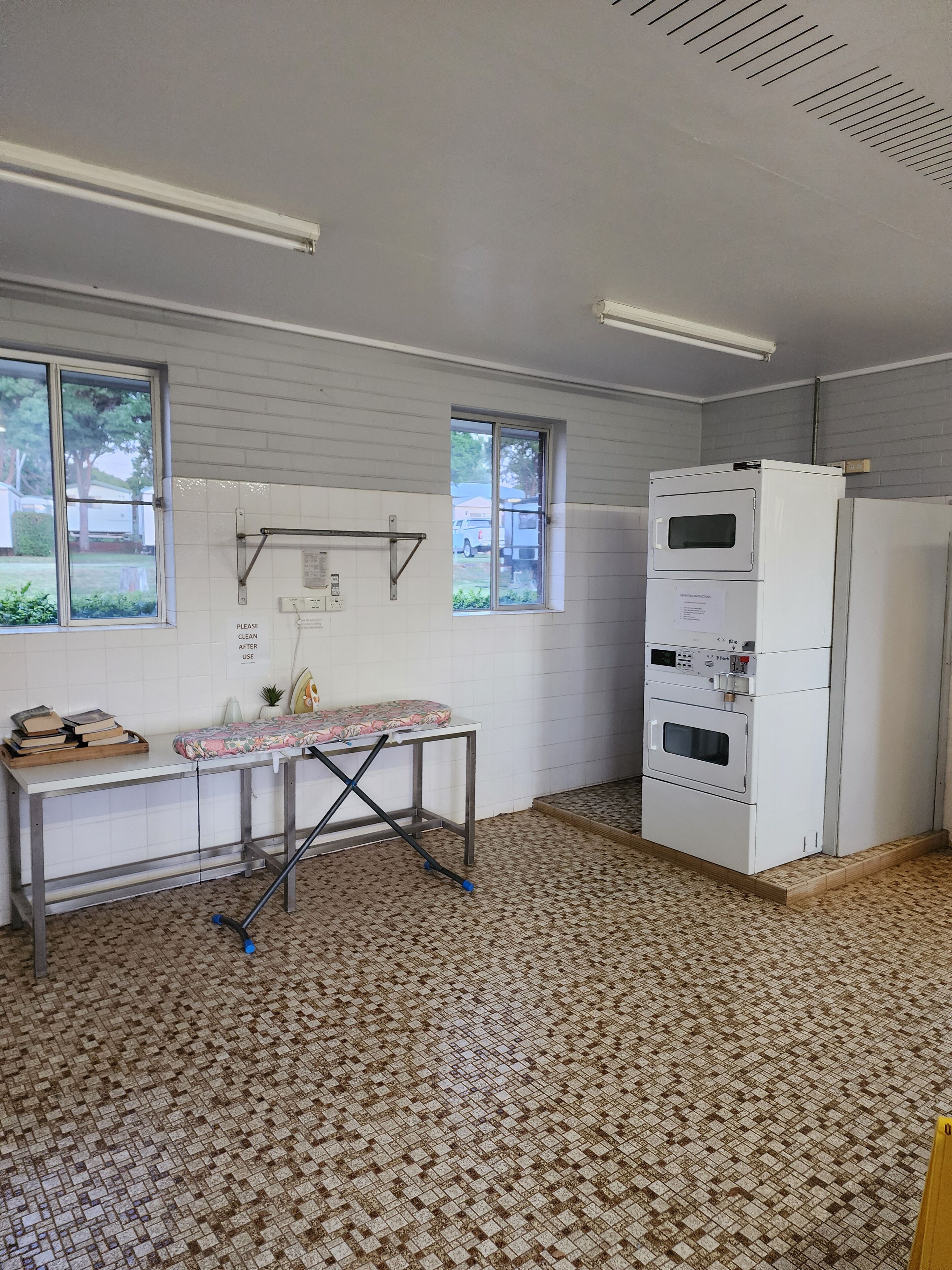 A room with a tiled floor, a table with a floral tablecloth, a white refrigerator, and a window with a view of a parked truck outside.