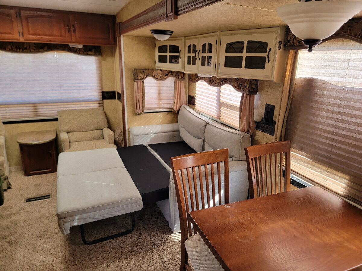 A compact RV interior with a bed, a dining table, and a seating area.