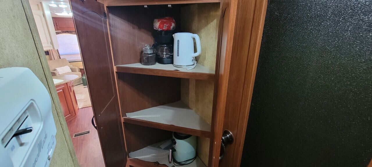 A wooden cabinet with shelves containing a white coffee maker, a kettle, and a jar.