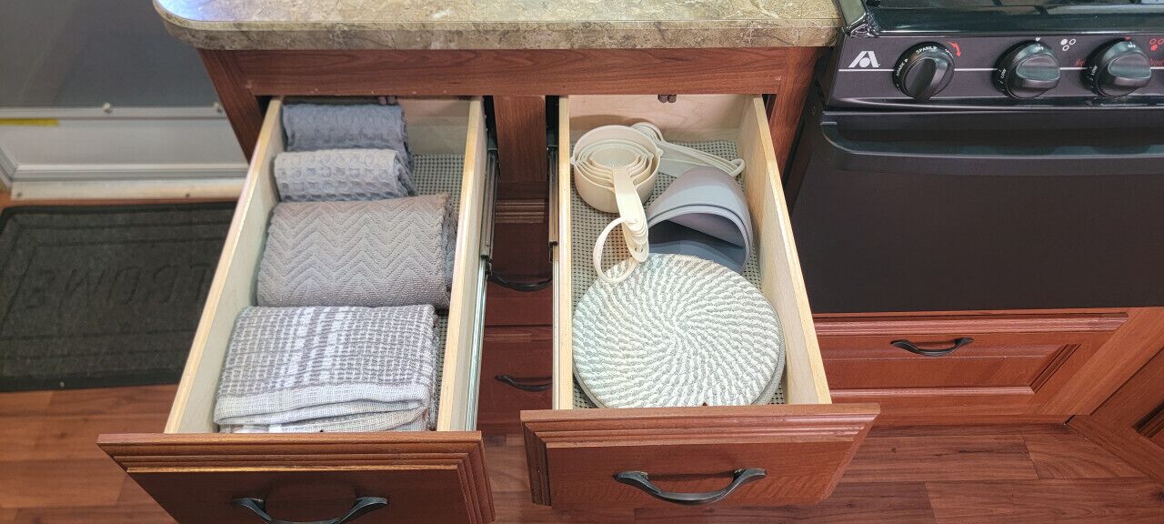 A kitchen drawer with neatly folded towels and a round woven mat.