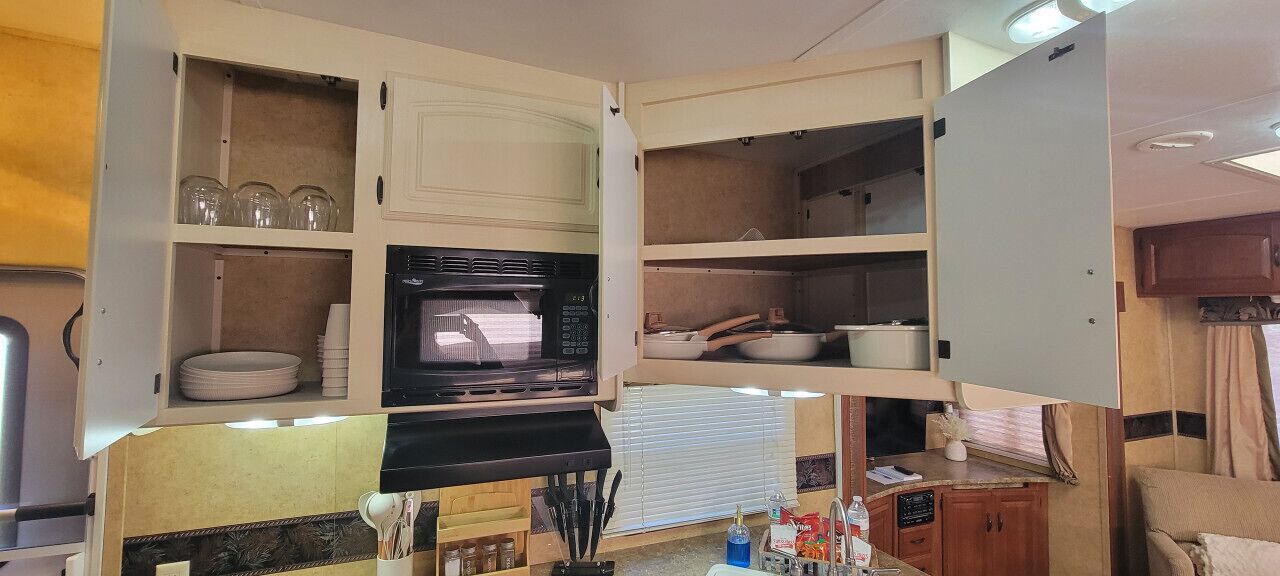 A compact kitchen with a microwave, stove, and various storage shelves.