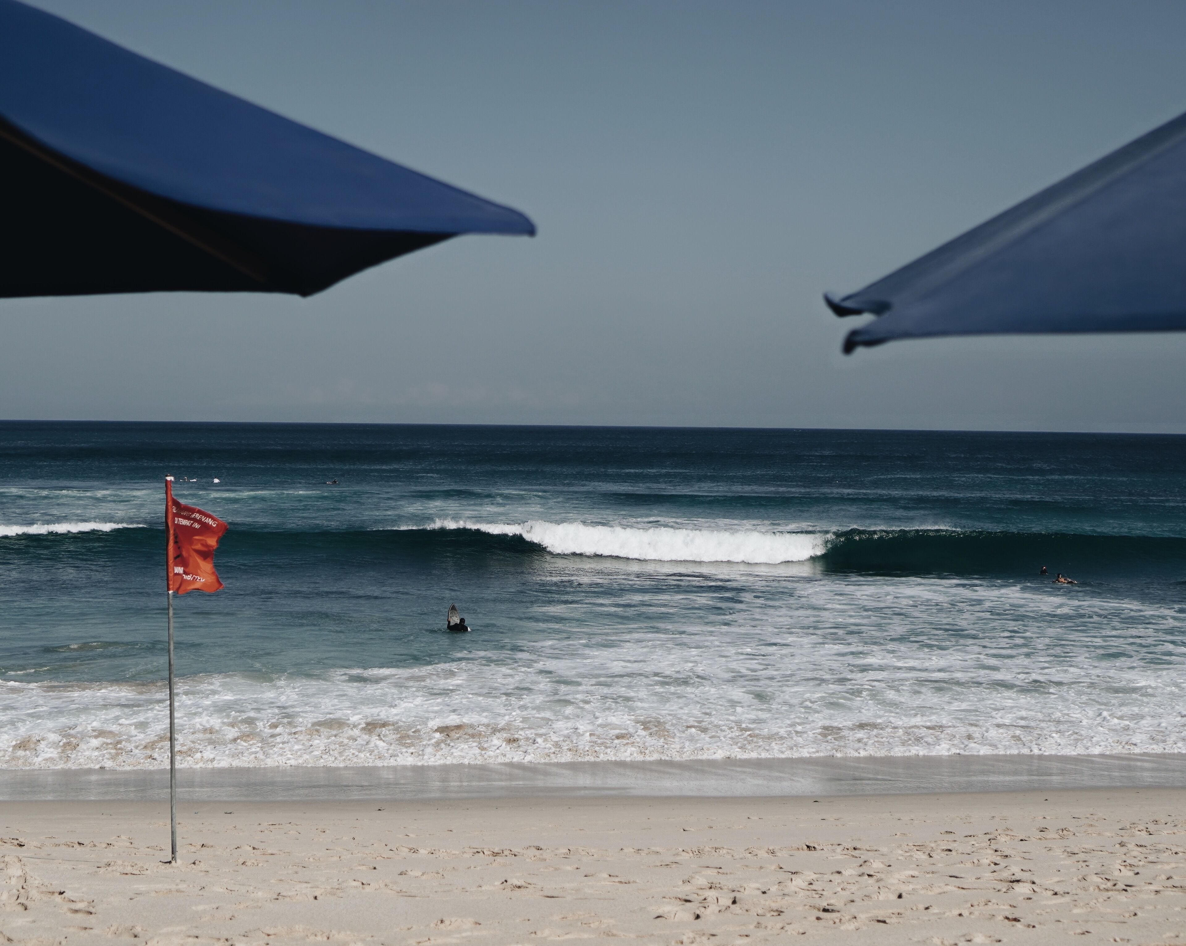 A beach with a flag, waves, and umbrellas.