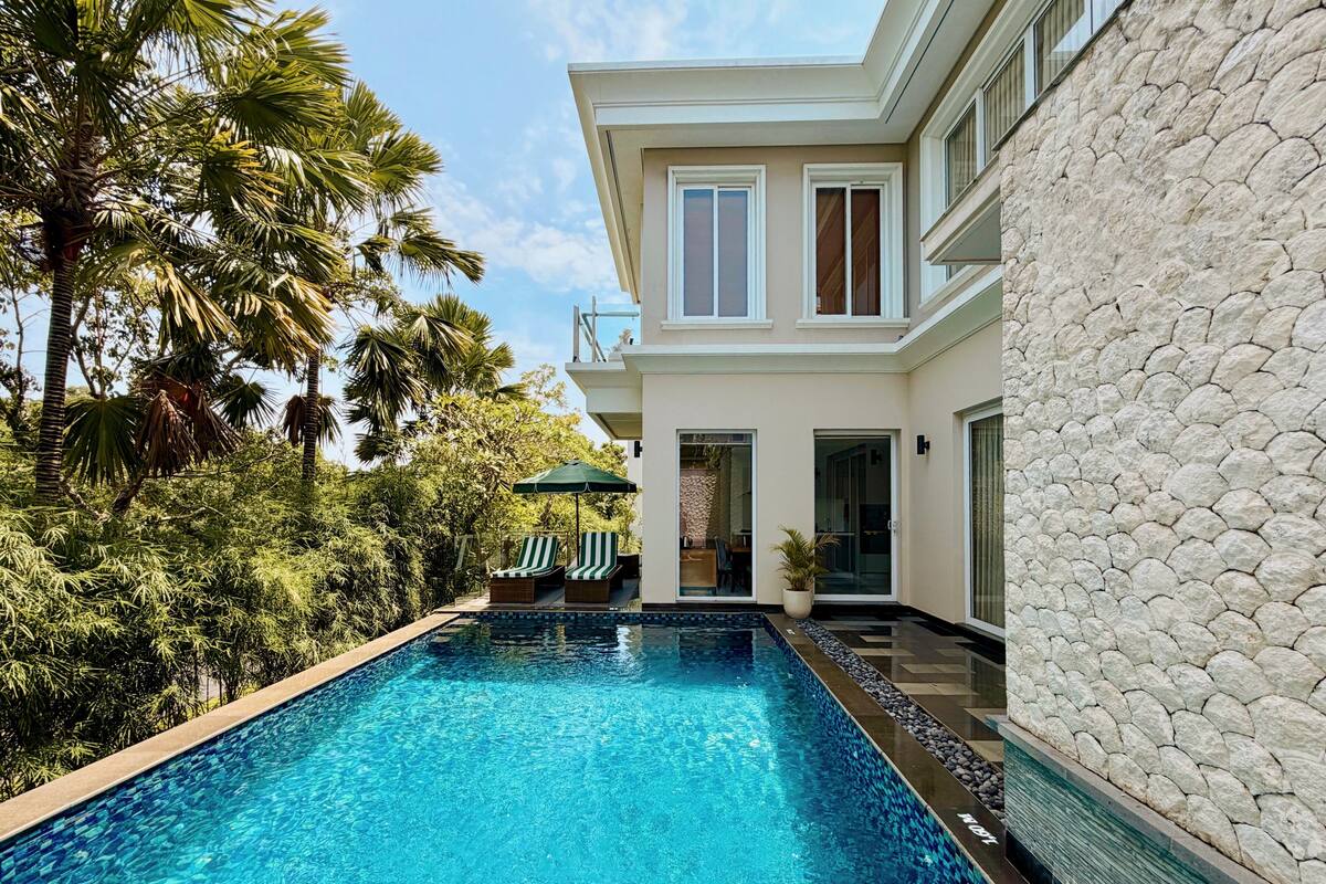 Una piscina con sillas de descanso, un muro de piedra y un edificio moderno con ventanas grandes.