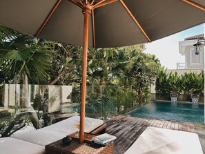 A poolside lounge area with wooden flooring, white lounge chairs, and an umbrella providing shade. - Kula Kara Villas Bingin, Uluwatu (Pecatu)