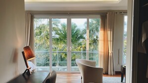Una habitación moderna con piso de madera, un ventanal con cortinas, una silla blanca y una lámpara.