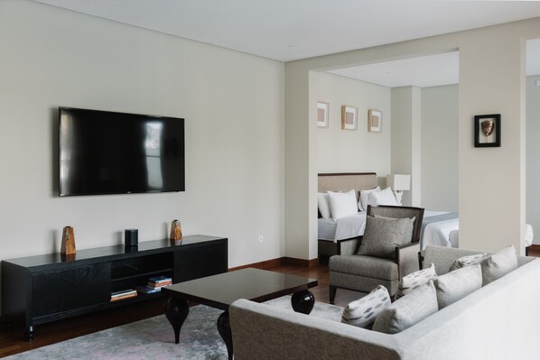 A modern living room with a flat-screen TV, a dark wooden entertainment unit, a grey sofa, and a matching armchair.