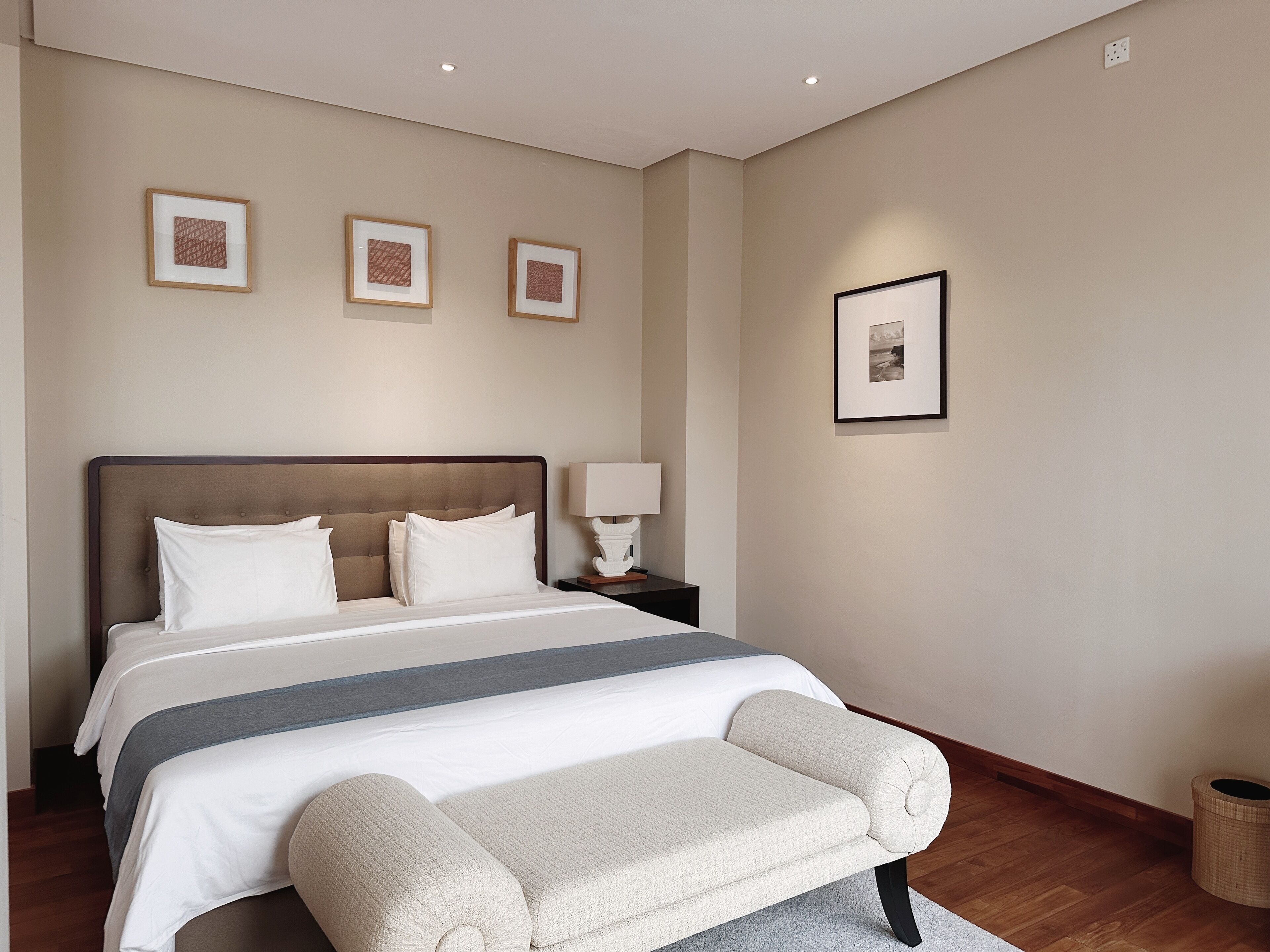 Una habitación de hotel ordenada con una cama grande, una mesita de noche con lámpara y tres cuadros en la pared.
