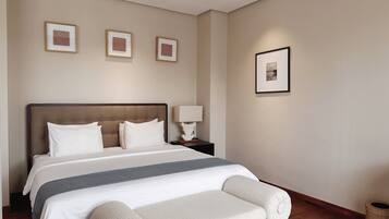 Una habitación de hotel ordenada con una cama grande, una mesita de noche con lámpara y tres cuadros en la pared.