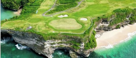 An aerial view of a golf course with a beach and cliffs.