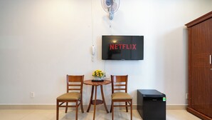 A room with a TV mounted on the wall, two wooden chairs, a small table with a vase, and a black appliance. - Green Airport Hotel (Ho Chi Minh City)