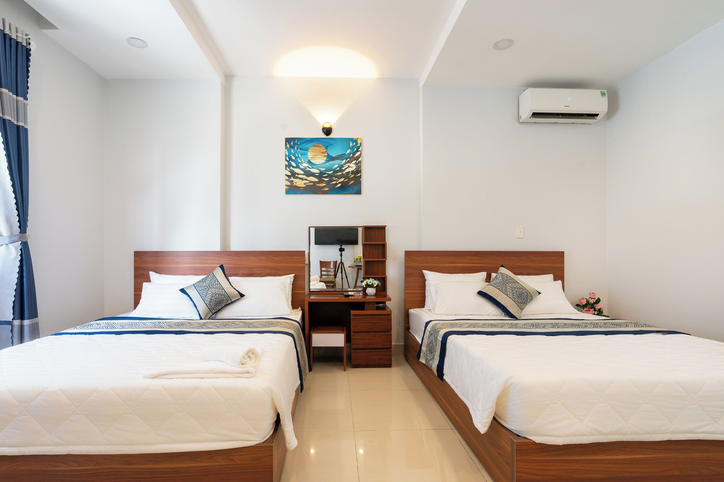 Quarto de hotel com duas camas, uma escrivaninha, uma cadeira, um espelho, ar condicionado e um quadro na parede.