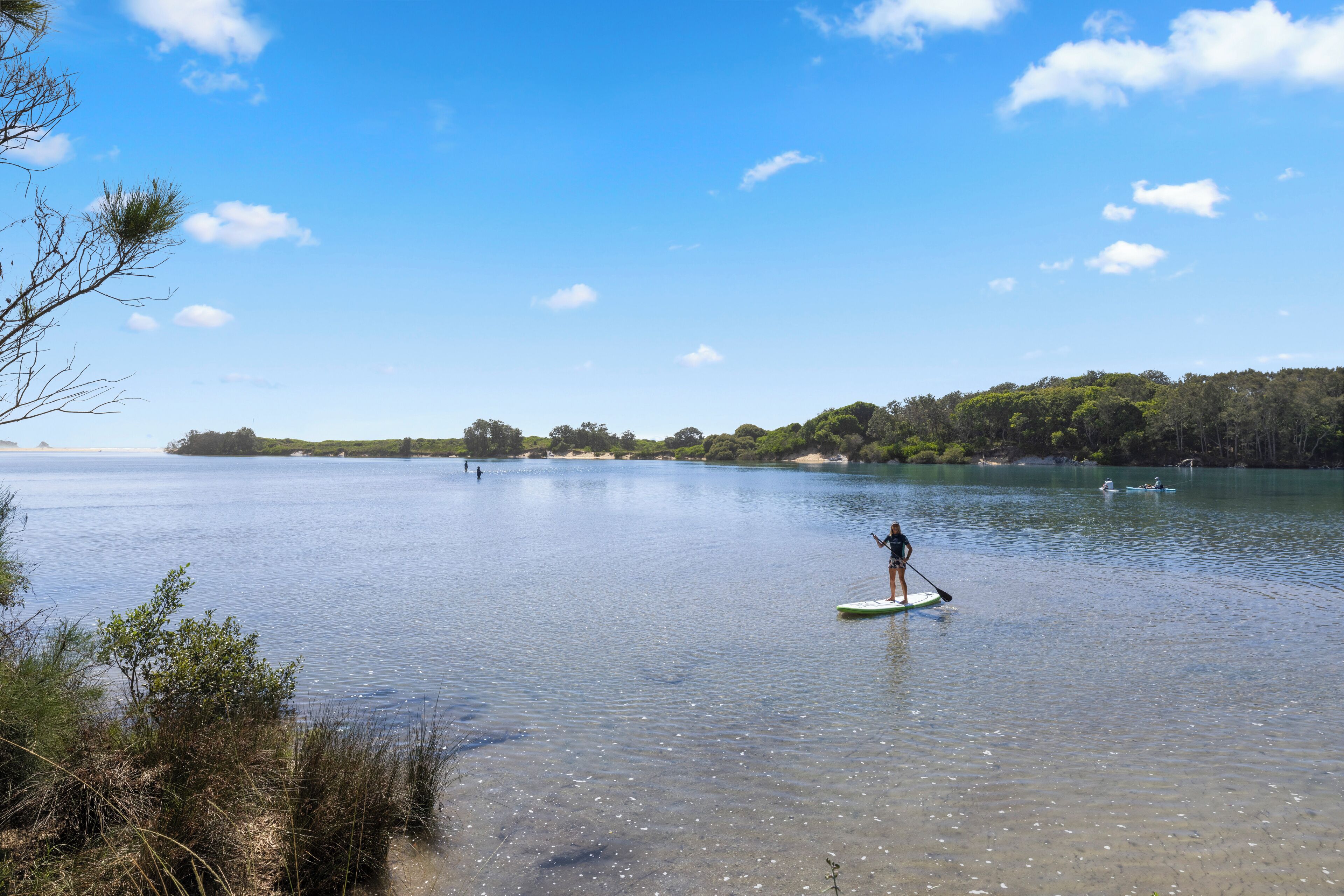 A calm lake with a person paddleboarding, surrounded by trees and clear skies.