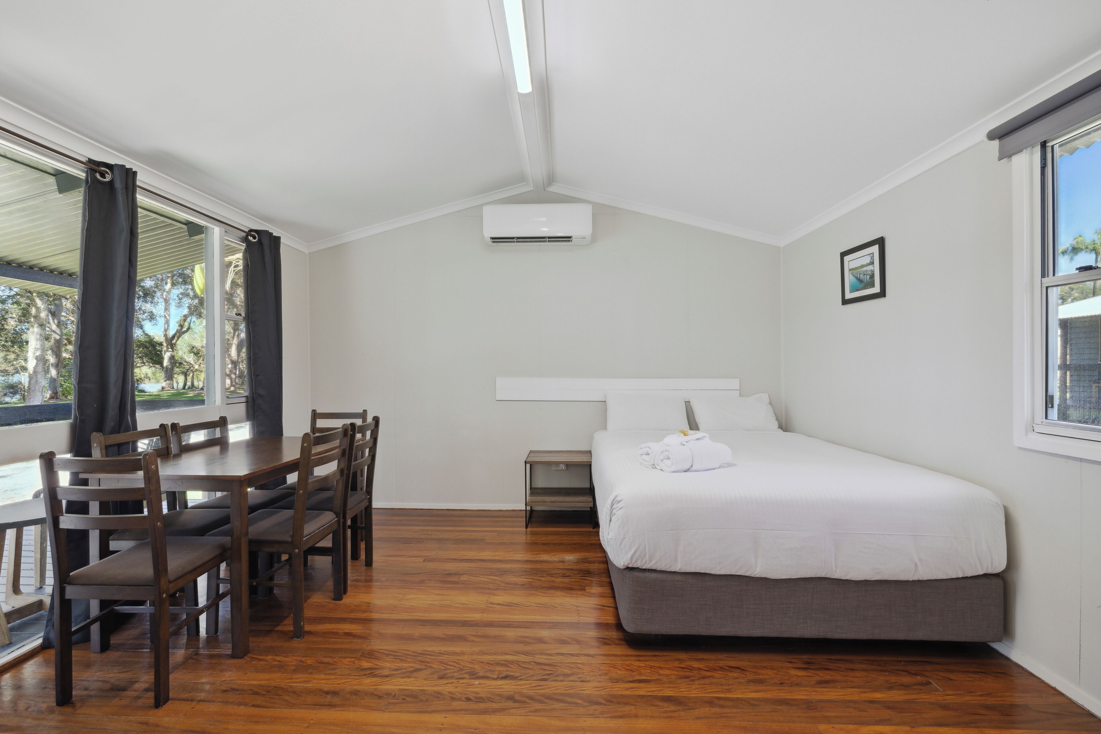 Un dormitorio con cama, escritorio, sillas, ventana y unidad de aire acondicionado.