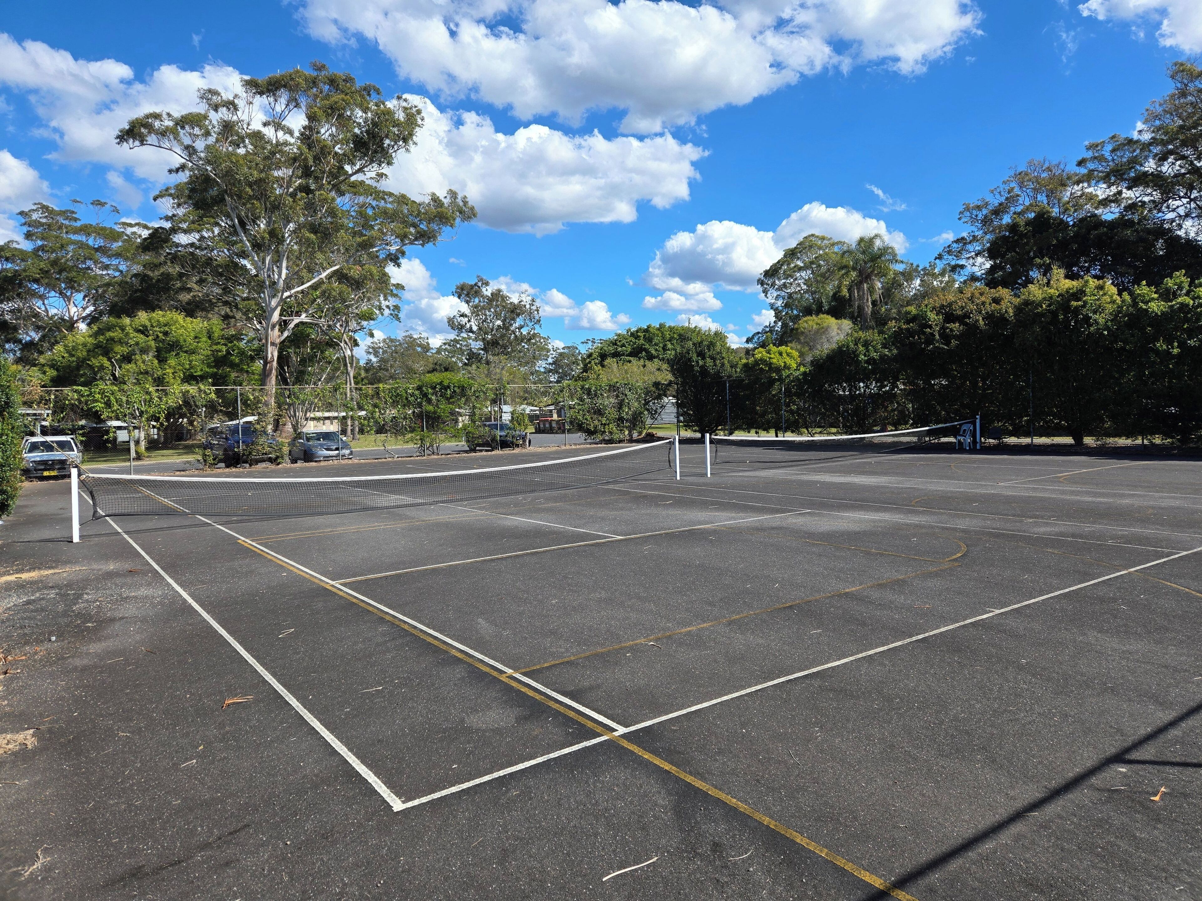 A tennis court with a net, surrounded by trees and parked cars.