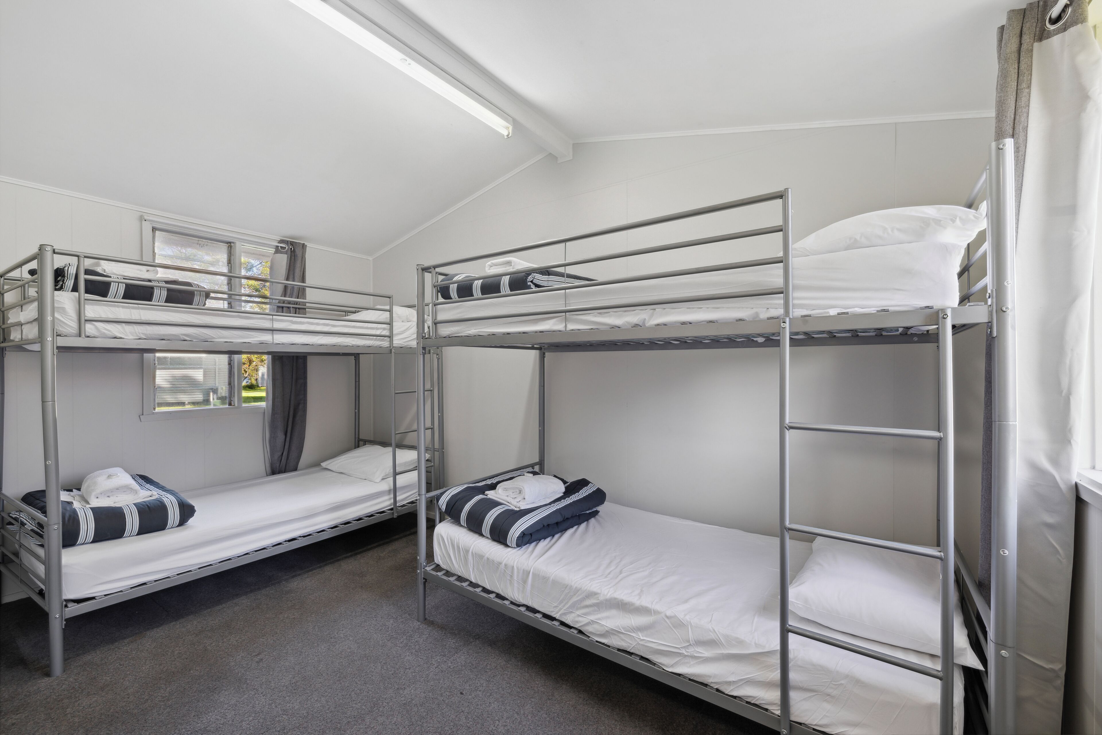 Ein Schlafsaalzimmer mit zwei Etagenbetten, jeweils mit Kissen und zusammengefaltetem Bettbezug.