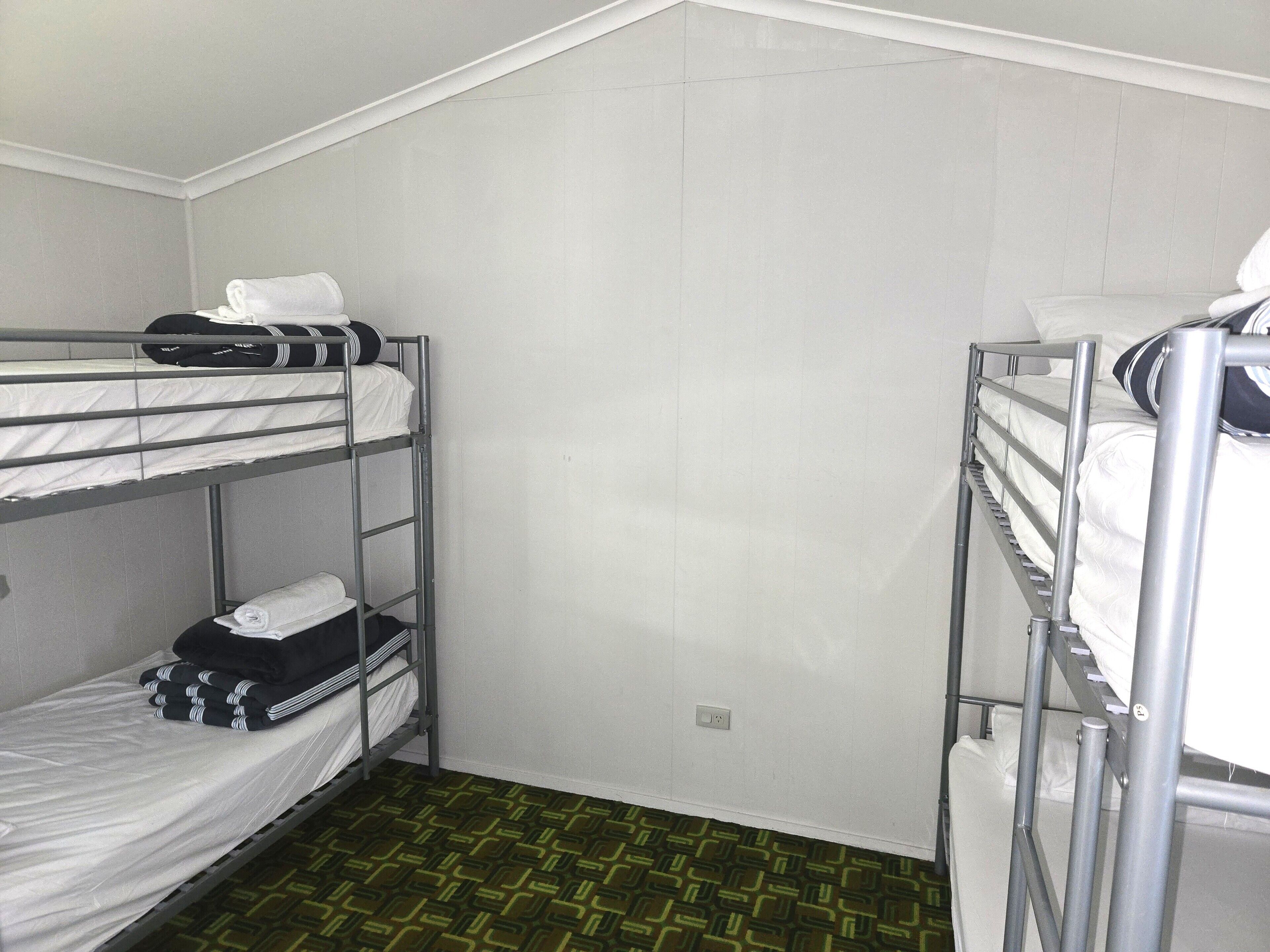 A dormitory room with bunk beds, a patterned floor, and a plain wall.