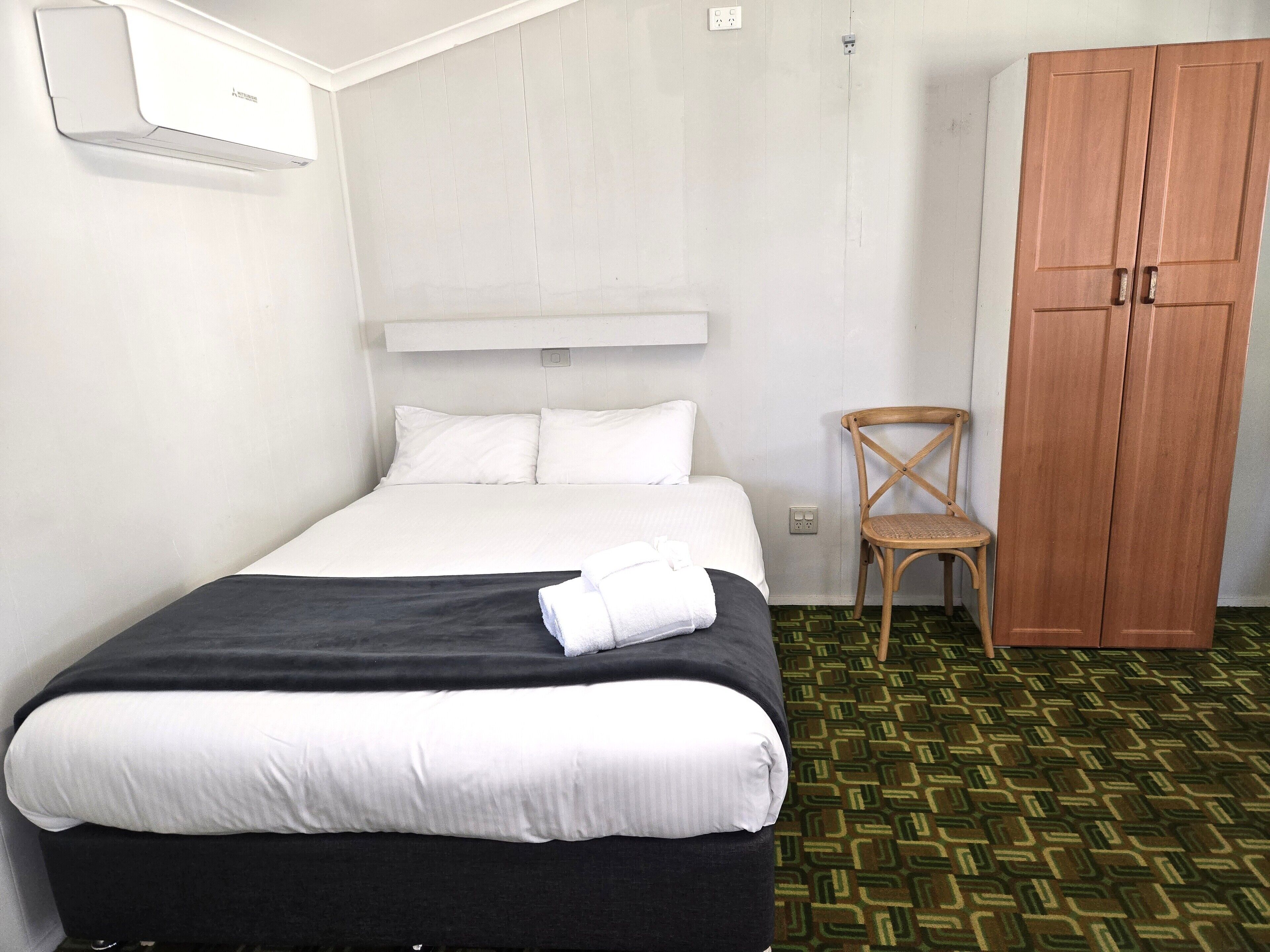 Habitación de hotel con una cama, un armario de madera, una silla y un equipo de aire acondicionado.