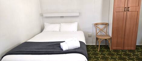 Habitación de hotel con una cama, un armario de madera, una silla y un equipo de aire acondicionado.