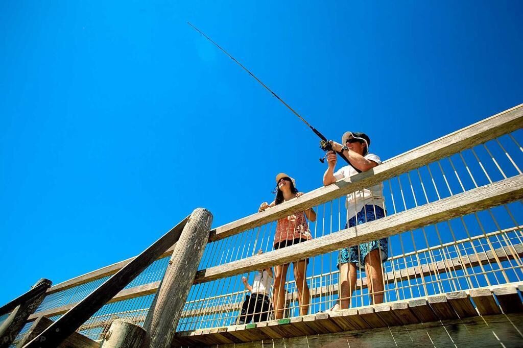A wooden pier with a metal railing, a clear blue sky, and people fishing.