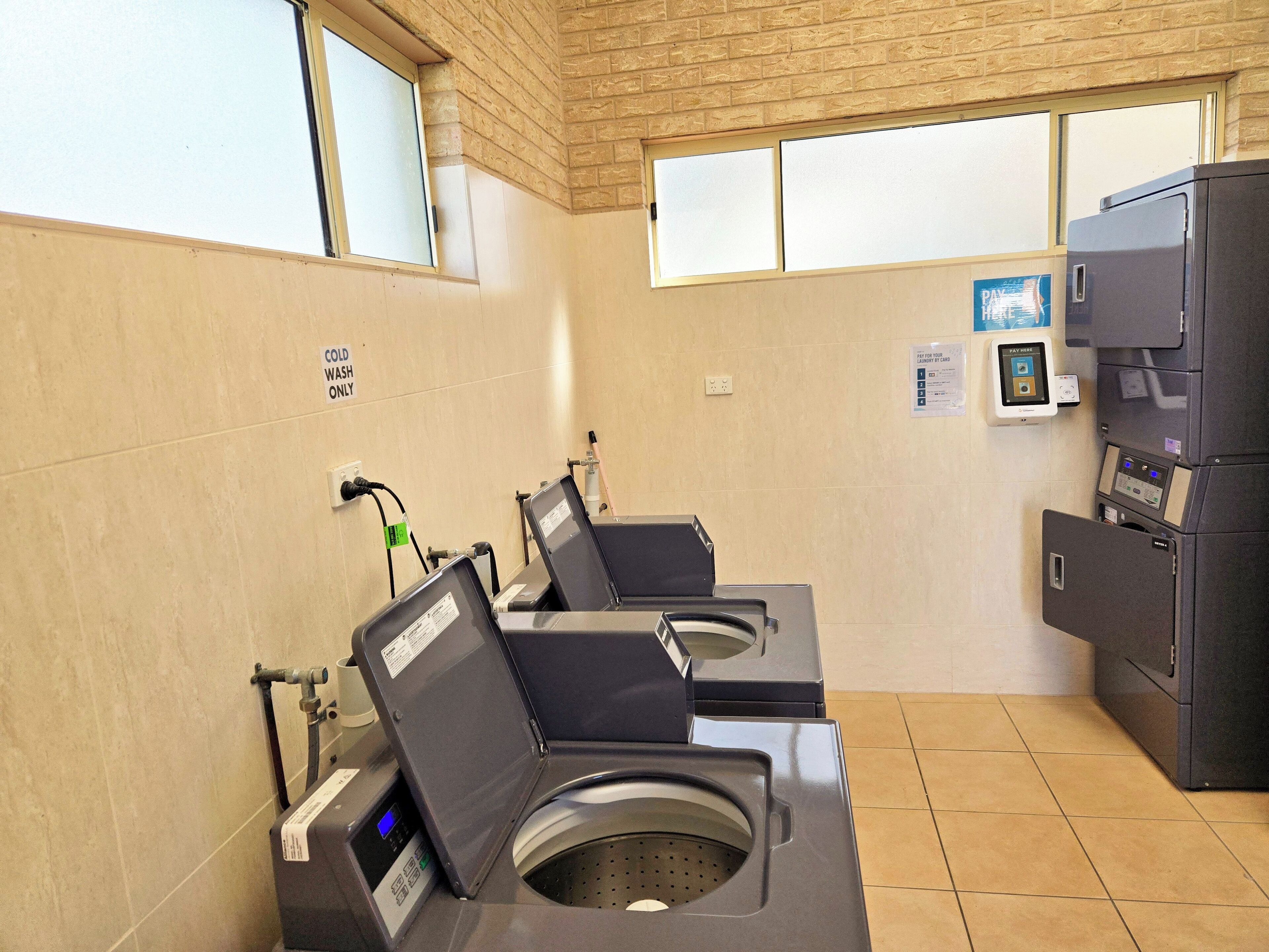 A public laundromat with two front-loading washing machines, a dryer, and a payment kiosk.