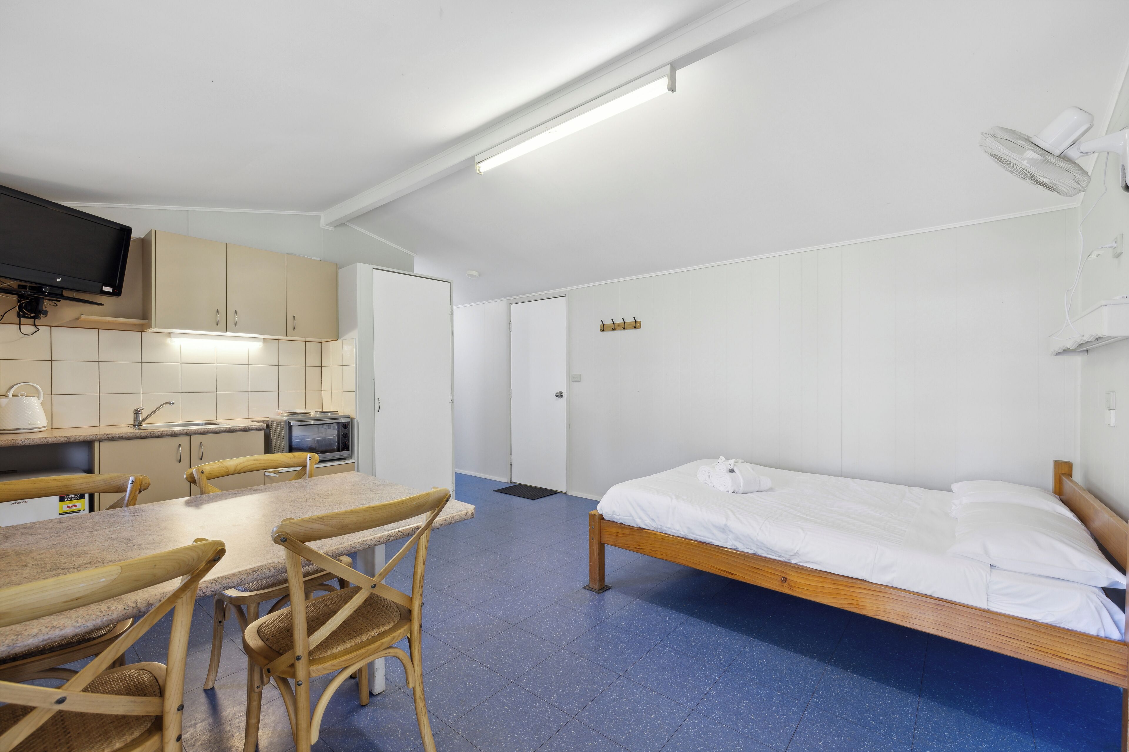 A room with a bed, a table with chairs, a microwave, a television, and a fan.