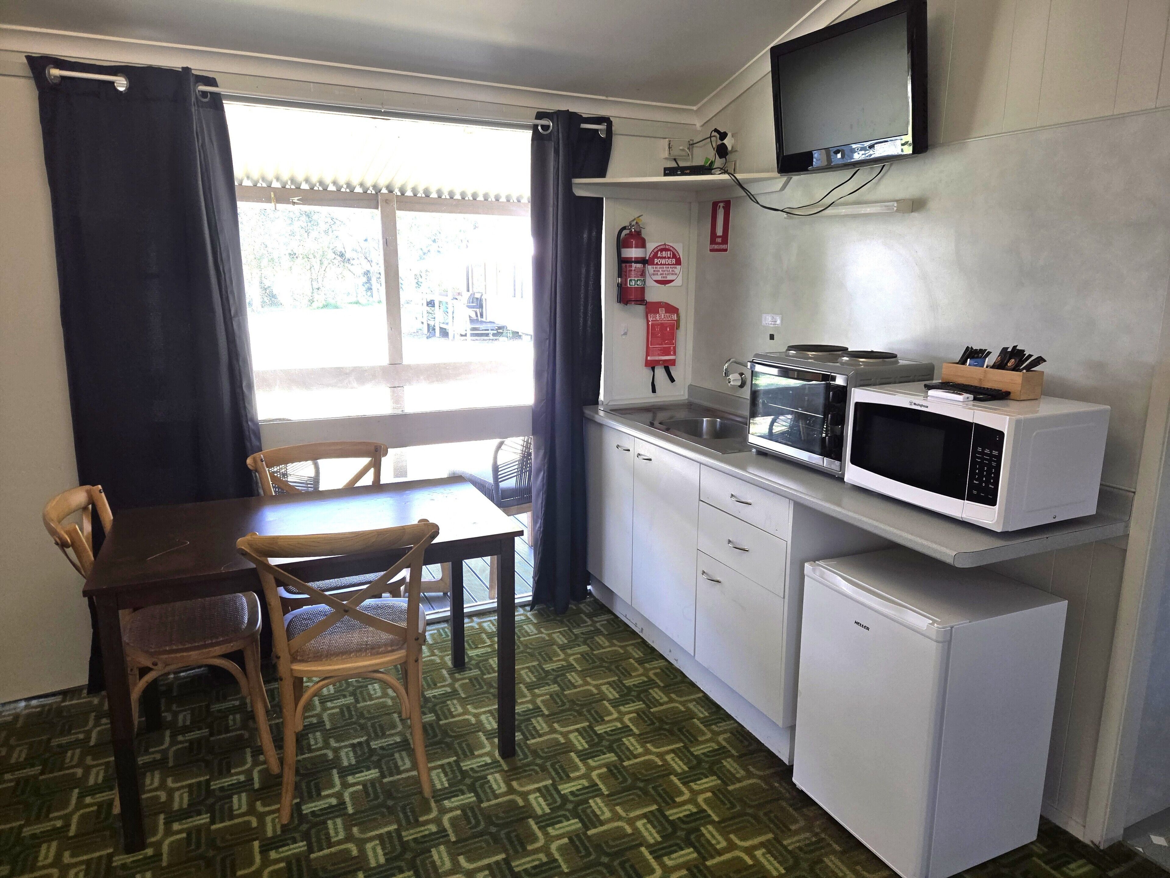 Cocina compacta con mesa, sillas, microondas, refrigerador pequeño y televisor en la pared.