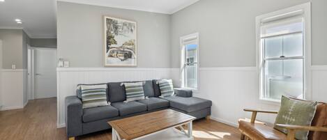 A modern living room with a grey sectional sofa, a wooden coffee table, a leather armchair, and a ceiling fan.