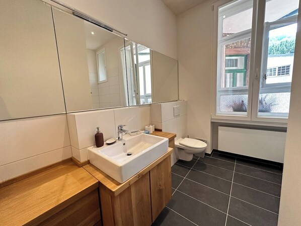 A modern bathroom with a large mirror, a sink, and a toilet.